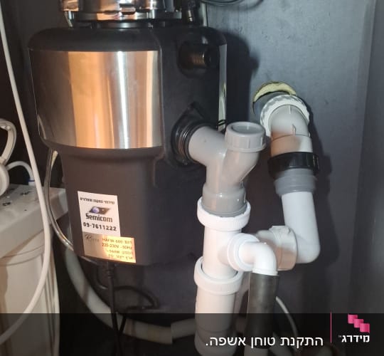 מתקן טוחן אשפה עם צינורות חיבור מתחת לכיור